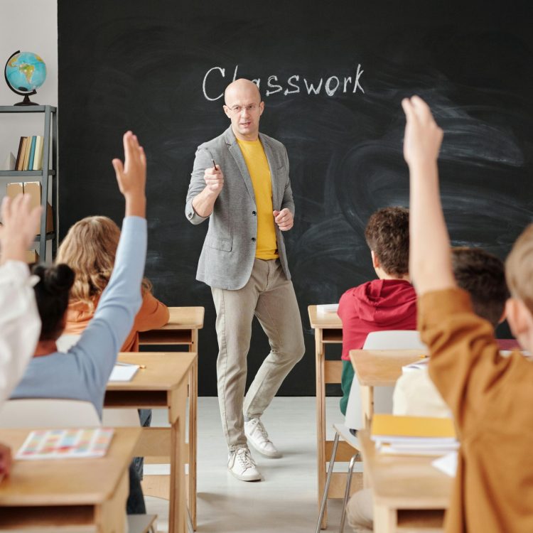 Teacher interacting with students raising hands in a classroom setting.
